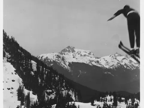 An old black and white photograph of a ski jumper flying high above the snow at Heather Meadows.