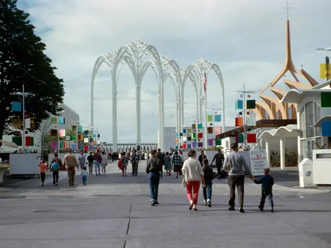 Fairgoers walk across a plaza toward tall white arches at the 1962 Seattle World's Fair.